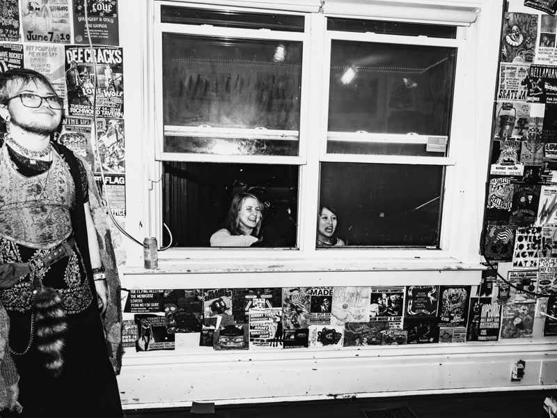 Photo of fans taking in a concert at the Probably House. We see outside of the window two fans looking in to see the show.